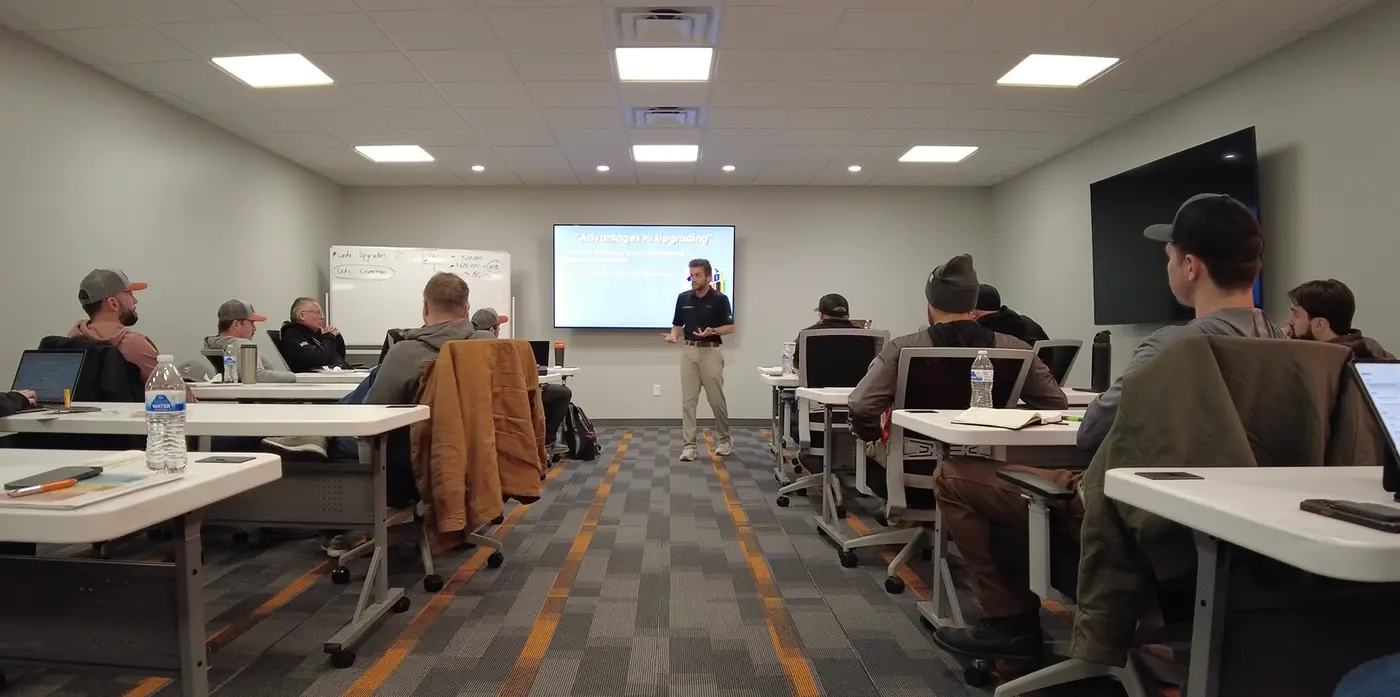 Noah at the front of the BCS Roofing training room with the team at their desks